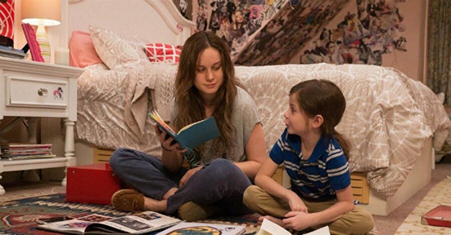 Gizli Dünya / Room (2015) IMDb 8.2

                                    
                                    5 yaşındaki bir çocuk, Jack (Jacob Tremblay) ve onun 24 yaşındaki genç annesi Ma (Brie Larson), küçük bakımsız bir evde yaşamaktadır. "Oda" olarak adlandırılan ve penceresiz, sadece tavanında ışıklığı olan bu evde Yaşlı Nick (Sean Bridgers) denilen bir adamın esiri olarak hayatını sürdürmektedirler ve asla dışarı çıkmamaktadırlar. Ma, şu ana kadar Jack'i durumun gerçekliğinden korumuştur fakat Jack 5. doğum gününde olayı artık anlamaya başlar ve Ma artık onun yaşının yeterli olduğunu düşünüp ona bir kaçış planı sağlar. Ma, Yaşlı Nick'in işten kovulduğunu öğrenir ve bunun onların güvenliğini etkilemekte olacağını bilmektedir. Ma, Jack'in kilit ortaklığıyla beraber planını etkinleştirir. Ma, dış dünya ile ilgili tüm gerçekleri anlatır. Jack'e ölü taklidi yapmasını öğretir ve Yaşlı Nick'i kandırıp gömülmesini sağlayacağını söyler. Yaşlı Nick olanlara inanır. Jack'i kamyonetine alıp yolun aşağısına doğru sürmeye başlar. Yolculuk sırasında Jack kaçmayı başarır. Sonra güvenli bir şekilde polise gider ve Ma'nın nerelerde olabileceğini hayal meyal anlatır. Kısa süre sonra Ma bulunur ve esir tutulduğu yerden kurtarılır. Ma ile Jack ağlayarak kavuşurlar. Hastanede geçirilen kısa bir sürenin ardından Ma, Jack'i alır ve anne babasının evine götürür. Ailenin birleşiminden sonra Ma'nın annesi (Joan Allen) ve babası (William H. Macy) arasında sorunlar ortaya çıkar. Jack eski odasının dışındaki hayatına alışmakla mücadele vermekte ve sadece annesiyle konuşmaktadır. Eski evindeki odasına dönmeyi istediğini anlatır. Ma yaşadığı sıkıntılarla depresyona girer, hastaneye kaldırılır. Bu sırada Jack dış dünyaya alışır. Annesine kendisinden bir parça vererek ona güç vereceği umuduyla Jack büyükannesinden saçını kestirip Ma'ya vermesini ister. Ma iyileşip geri döndüğünde Jack'ten özür diler ve hayatını kurtardığı için tekar teşekkür eder. Jack'in isteği üzerine Jack ve Ma son defa Oda'ya gider. Jack ve Ma, Oda ile vedalaşır.

 Lenny Abrahamson'un yönettiği ve senaryosunu Emma Donoghue'nun yazdığı aynı adlı kitaptan uyarladığı 2015 Kanada-İrlanda yapımı dram filmi olan Gizli Dünya'nın oyuncu kadrosunda Brie Larson, Jacob Tremblay, Joan Allen, Sean Bridgers ve William H. Macy oynamaktadır. 88. Akademi Ödülleri'nde 4 dalda aday gösterilen film Brie Larson'un oyunculuğuyla En İyi Kadın Oyuncu ödülünü kazanırken, 73. Altın Küre Ödülleri'nde ve 69. BAFTA Ödülleri'nde yine En İyi Kadın Oyuncu ödüllerini kazandı.
                                
                                