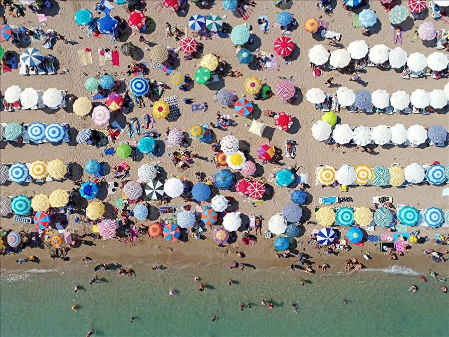Altınkum'da renk cümbüşü
Türkiye'nin deniz turizmi merkezlerinden Didim'deki Altınkum Plajı, ince kumu ve şehir merkezinde bulunması nedeniyle çok sayıda yerli ve yabancı turisti ağırlıyor. Kumunun renginden dolayı "Altınkum" adı verilen, bin 606 metre uzunluğunda ve 24 bin 103 metrekare büyüklüğündeki plaj, havadan yapılan çekimlerde renkli görüntüler yansıtıyor. Halka açık plaja vatandaşların güneşten korunmak için getirdiği farklı renklerdeki şemsiyeler, altın rengi kumlar üzerinde renk cümbüşü oluşturuyor. Plajı yer yer tamamen kaplayan şemsiyelerin hava çekimlerindeki görünümü, kumun üzerine sıralanmış boncukları andırıyor.