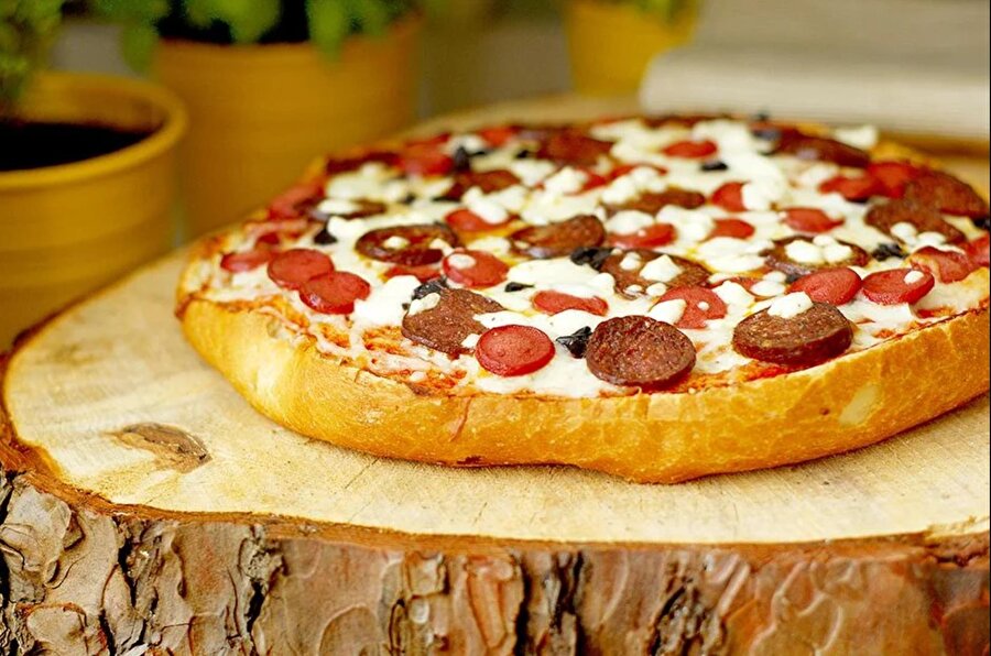 Bonus #1 Ekmek pizza

                                    
                                    Bu pizza tarifi hem midenize hem vicdanınıza iyi gelecek. Bayatlamış ekmekleri çöpe atmak yerine harika bir lezzete dönüştürmek artık sizin elinizde. Pizza restoranlarına taş çıkaracak kalitede bir pizza tarifi adı da hazır 'pizzamek'.

  
- Gerekli malzemeler:

  
1) 1 adet bayat ekmek(yatay olarak iki eşit parçaya bölünmüş)

  
Ekmek sosu için:

  
1) 4 adet orta boy domates

  
2) 2 yemek kaşığı domates salçası

  
3) 1 çay kaşığı kekik

  
4) 2 çay kaşığı tuz

  
5) 1 yemek kaşığı tereyağı (oda sıcaklığında bekletilmiş) 
  
Pizza üstü için gerekli malzemeler:

  
1) 100 gram mozzarella peyniri

  
2) 100 gram sucuk

  
3) 100 gram salam4) 100 gram rendelenmiş kaşar peyniri 
  
5) 100 gram beyaz peynir 
  
6) 2 yemek kaşığı doğranmış siyah zeytin 
  
*Püf noktası

  
Pizzamız sarı buğday ekmeğiyle çok daha lezzetli oluyor.Pizzayı dilediğiniz malzemeleri ekleyerek daha de zenginleştirebilir, malzeme listesinde yer alan ürünleri arzu ettiğiniz miktarlarda kullanabilirsiniz. 
  
- Ekmekli pizzanın yapılışı - 
  
1. Pizza sosunu hazırlamak için; kabuklarını soyduğunuz domatesleri iri küpler halinde doğrayın. 

  
2. Domates salçası, kekik, fesleğen ve tuz ilave ettiğiniz domates küplerini mutfak robotunda püre haline getirin.

  
3. Hazırladığınız sosu, yatay olarak kestiğimiz ekmeklerin üzerine sürün. Kenarlarına da biraz oda sıcaklığında bekletilmiş tereyağı dokundurmayı unutmayın. 
  
4. Sırayı bozmayacak şekilde; mozzarella peyniri, sucuk, salam, jambon dilimleri, rendelenmiş kaşar peyniri ve doğranmış siyah zeytini ekmek dilimleri üzerine serpiştirin. 
  
5. Önceden ısıtılmış 200 derece fırına sürün ve üstündeki kaşar peyniri kızarmaya başlayana kadar (hafif renk değiştirecek) pişirin. 

  
6. Daha sonra dışarı çekip üzerine ufaladığınız beyaz peyniri serpiştirin ve tekrar fırına sürün. Beyaz peynir eridiğinde pizzanız olmuş demektir.

  
7. Bayat ekmek dilimlerini değerlendirerek hazırladığınız ekmek pizzaları, sevdiklerinizle birlikte afiyetle yiyebilirsiniz.
                                
                                