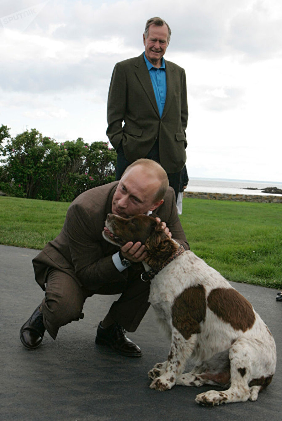 
                                    Vladimir Putin, ABD ziyareti sırasında bir köpeği severken görünüyor. Arkasında ise dönemin ABD Başkanı George H. W. Bush duruyor.
                                