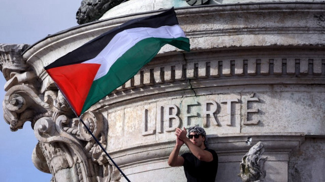 Un manifestant applaudit près du drapeau palestinien sous l'inscription "Liberté" au sommet du Monument à la République lors d'une manifestation appelant à la paix à Gaza, place de la République à Paris, le 22 octobre 2023. Crédit photo: EMMANUEL DUNAND / AFP
