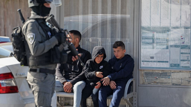 La police d'occupation israélienne près des enfants Palestiniens assis sur un banc d'un arrêt de bus pendant la prière du vendredi dans le quartier de Ras al-Amud en Palestine, le 1er décembre 2023. Crédit photo: AHMAD GHARABLI / AFP
