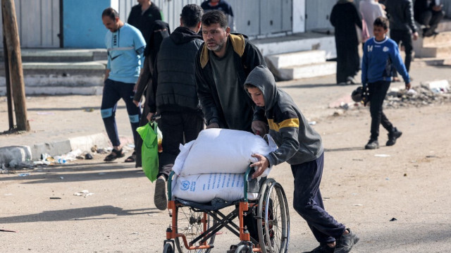 Un homme et un garçon poussent un fauteuil roulant transportant des sacs de farine que leur famille a reçus d'un entrepôt de l'Office de secours et de travaux des Nations Unies pour les réfugiés de Palestine (UNRWA) à Rafah, dans le sud de la bande de Gaza, le 12 décembre 2023.