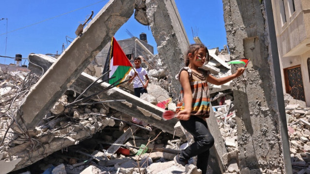 Des enfants palestiniens agitent des drapeaux nationaux palestiniens alors qu'ils jouent parmi les décombres de bâtiments détruits par les bombardements israéliens du mois dernier dans la bande de Gaza, à Khan Younès, dans le sud de la bande de Gaza, le 19 juin 2021.