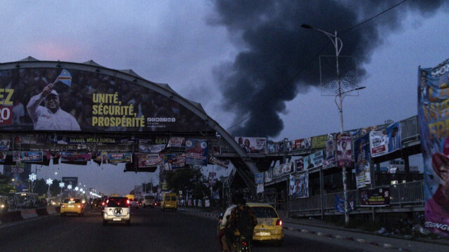 Une bannière de campagne du président de la République démocratique du Congo, Félix Tshisekedi, est photographiée alors que la fumée d'un réservoir de carburant en feu est visible à Kinshasa, le 16 décembre 2023.