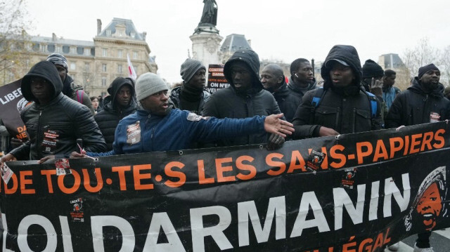 Des manifestants se tiennent derrière une banderole lors d'une marche de solidarité pour la défense des immigrés contre la nouvelle loi française sur l'immigration, place de la République à Paris, le 22 décembre 2023.