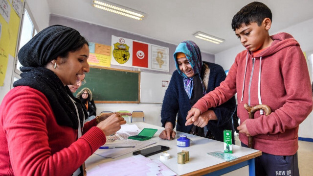 Une électrice est aidée à tremper son doigt dans l'encre après avoir voté dans un bureau de vote lors des élections locales de 2023 dans la localité de Mnihla dans la province d'Ariana, à la périphérie de Tunis, le 24 décembre 2023.