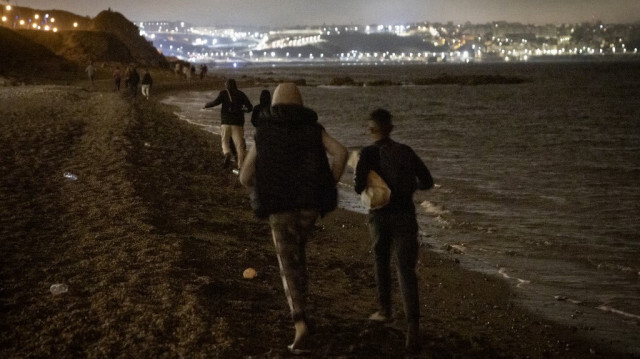 Les migrants marocains marchent sur le bord de la mer vers une falaise rocheuse dans la ville septentrionale de Fnideq alors qu'ils tentent de traverser la frontière entre le Maroc et l'enclave nord-africaine espagnole de Ceuta le 18 mai 2021.