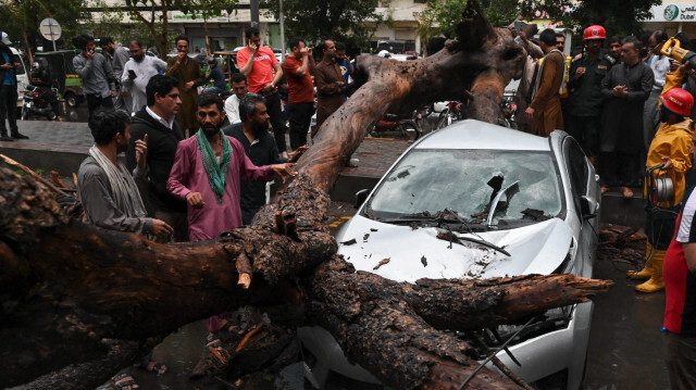 Des personnes se rassemblent autour d'une voiture endommagée par la chute d'un arbre lors d'une averse à Lahore, le 6 juin 2023. Crédit Photo: Arif ALI / AFP

