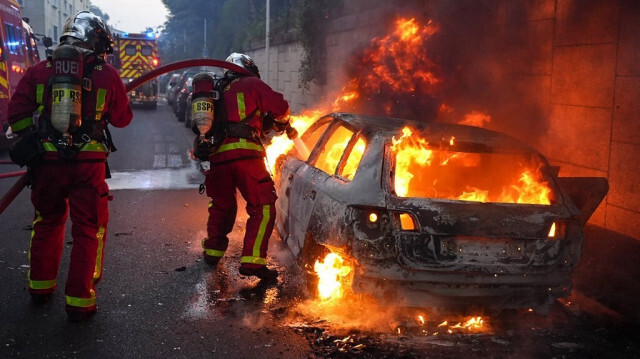 Des pompiers s'efforcent d'éteindre une voiture en feu en marge d'une manifestation à Nanterre, à l'ouest de Paris, le 27 juin 2023, après que la police française a tué un adolescent qui avait refusé de s'arrêter pour un contrôle routier. Crédit photo: ZAKARIA ABDELKAFI / AFP