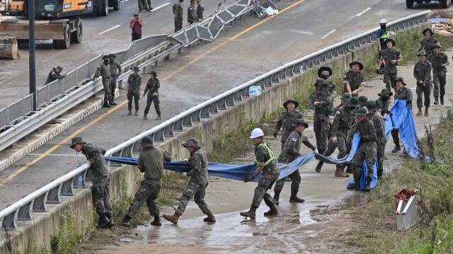 Des soldats sud-coréens transportant un tube pour pomper l'eau d'un tunnel le long d'une route menant à un tunnel souterrain où une quinzaine de voitures ont été piégées par les eaux d'inondation après de fortes pluies à Cheongju, le 16 juillet 2023. Crédit Photo: JUNG YEON-JE / AFP

