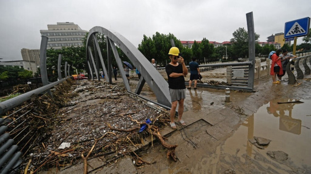 Des gens marchent le long d’une rue remplie d’eau, après de fortes pluies dans le district de Mentougou à Pékin en Chine. Crédit photo: PEDRO PARDO / AFP