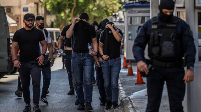 Les supporters de football se couvrent le visage en quittant le quartier général de la police d'Athènes, le 11 août 2023, alors qu'ils sont détenus dans le cadre de l'enquête sur la mort de Michalis Katsouris. Crédit photo: ANGELOS TZORTZINIS / AFP

