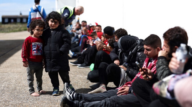 Deux enfants photographiés aux côtés de migrants qui attendent le bus pour être pris en charge, à Dungeness, sur la côte sud-est de l'Angleterre, le 16 août 2023. Crédit photo: HENRY NICHOLLS / AFP
