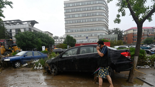 Un homme passant devant des voitures endommagées par de fortes pluies dans le district de Mentougou à Pékin. Crédit Photo: Pedro PARDO / AFP

