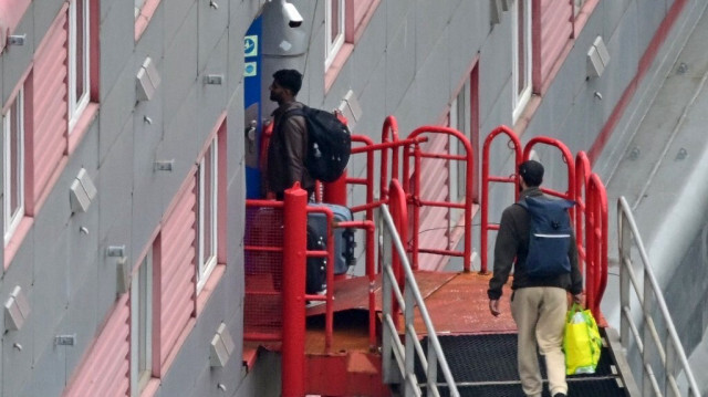 Des personnes portant des sacs remontent le couloir d'accès à la barge d'hébergement Bibby Stockholm, amarrée au quai du port de Portland, sur la côte sud-ouest de l'Angleterre, le 7 août 2023. Crédit photo: BEN STANSALL / AFP
