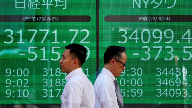 Des gens marchant devant un tableau électronique affichant la moyenne Nikkei de la Bourse de Tokyo et les chiffres du New York Dow le long d'une rue de Tokyo le 25 août 2023.