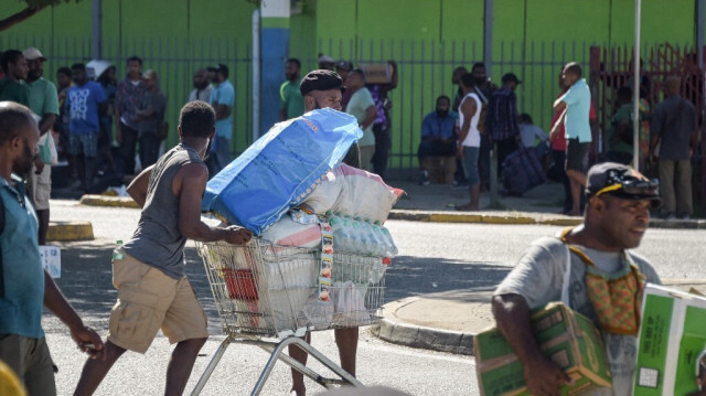 Un homme poussant un chariot dans la rue alors que les foules quittent les magasins avec des marchandises pillées au milieu d'un état de troubles à Port Moresby le 10 janvier 2024.