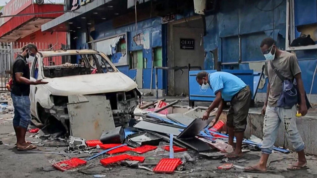 Des personnes en train de nettoyer les débris devant des bâtiments endommagés lors des émeutes à Port Moresby, le 11 janvier 2024.