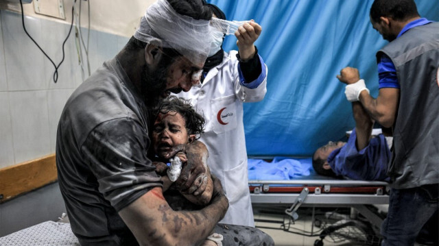 Un Palestinien tient dans ses bras un enfant tous deux gravement blessés, survivants aux bombardements israéliens, pendant qu'une infirmière lui fait un bandage à la tête dans le service de traumatologie de l'hôpital Nasser de Khan Younès, dans le sud de la Bande de Gaza, le 24 octobre 2023.