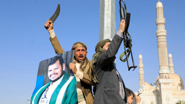 Des combattants huthis, dont l'un tient un portrait du dirigeant huthi Abdul Malik al-Houthi (à gauche), brandissant leurs armes lors d'une manifestation à la suite des frappes des forces américaines et britanniques, dans la capitale contrôlée par les huthis, Sanaa, le 12 janvier 2024, dans le contexte des batailles en cours entre Israël et le groupe Hamas à Gaza.