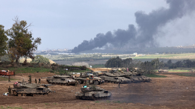 Des soldats israéliens se tenant à côté de chars dans une position en Israël près de la frontière avec la bande de Gaza, alors que de la fumée s'élève au-dessus de la bande de Gaza après un bombardement israélien, le 14 janvier 2024. 