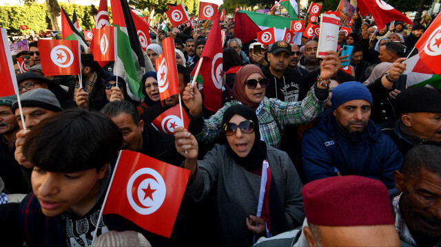 Des Tunisiens brandissant des drapeaux nationaux et palestiniens lors d'une manifestation marquant le 14e anniversaire de la révolution de 2011 et appelant à la libération des opposants au président sur l'avenue Habib Bourguiba à Tunis, le 14 janvier 2024.