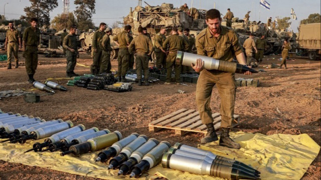 Un soldat de l'armée d'occupation transporte un obus lourd devant des chars de combat déployés sur une position le long de la frontière avec la bande de Gaza.