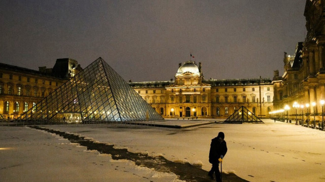 Un employé nettoie le sol enneigé du musée du Louvre à Paris, avec la pyramide du Louvre, conçue par l'architecte sino-américain Ieoh Ming Pei, en arrière-plan, le 18 janvier 2024.