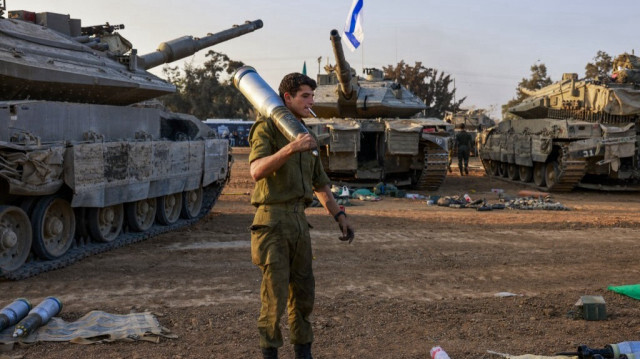 Un membre de l'armée d'occupation israélienne transportant un obus près des chars de combat déployés le long de la frontière avec la bande de Gaza, en Palestine, le 31 décembre 2023.