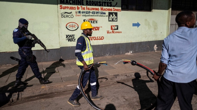 Un agent de sécurité privé porte son arme alors que des employés de Johannesburg City Power déplacent un gros câble en cuivre lors d'une opération avec le Département de la police métropolitaine de Johannesburg (JMPD) visant à couper les connexions électriques d'un immeuble résidentiel au quartier central des affaires de Johannesburg, le 20 septembre 2023.