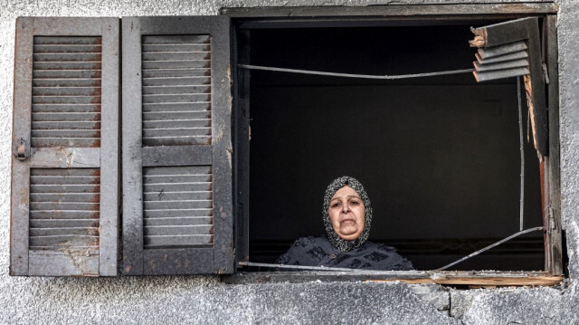 Une femme regarde par la fenêtre d'une maison endommagée située en face de celle où était abritée une famille palestinienne de Jabalieh déplacée à la suite d'un bombardement israélien à Rafah, dans le sud de la bande de Gaza, le 3 janvier 2024.