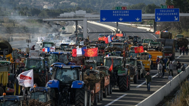 Des agriculteurs protestent avec des tracteurs pour bloquer l'autoroute A9 sous un panneau indiquant la direction de la frontière franco-espagnole et de Barcelone, près du péage de la Croix Sud à Narbonne, le 26 janvier 2024.