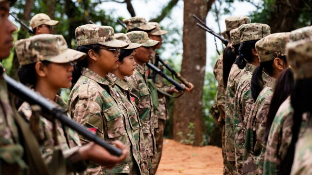 Photo prise le 8 décembre 2023 montrant des membres féminines des Forces de défense du peuple de Mandalay (MDY-PDF) en formation pour hisser le drapeau dans leur camp de base dans la forêt près de la municipalité de Namhsan, dans l'État septentrional de Shan au Myanmar.