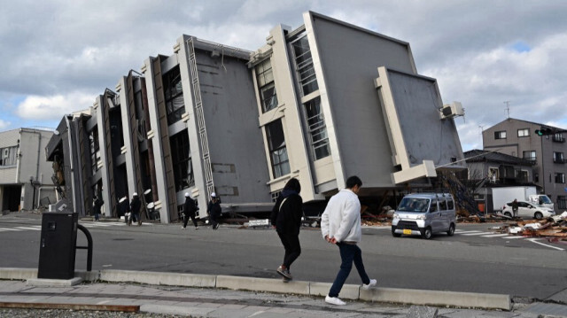 Des gens marchent devant un bâtiment effondré dans la ville de Wajima, préfecture d'Ishikawa, le 4 janvier 2024, après le séisme de magnitude 7,5 survenu dans la région de Noto dans la préfecture d'Ishikawa le jour de l'An. 
