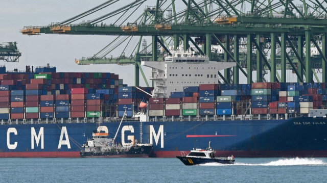 Un bateau navigue devant un navire porte-conteneurs amarré au terminal portuaire de Pasir Panjang à Singapour le 14 octobre 2022. 