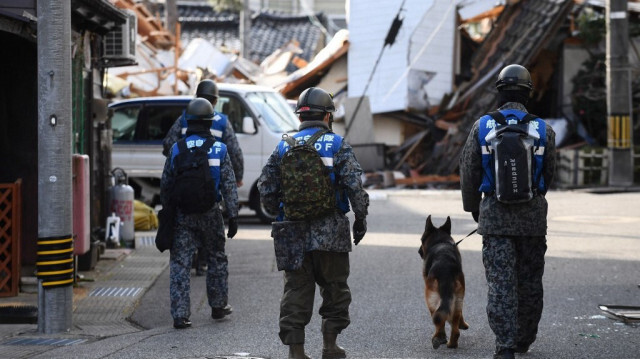 Des soldats de la Force d'autodéfense aérienne se promènent avec un chien pour rechercher des victimes du séisme dans la ville de Wajima, préfecture d'Ishikawa, le 5 janvier 2024.