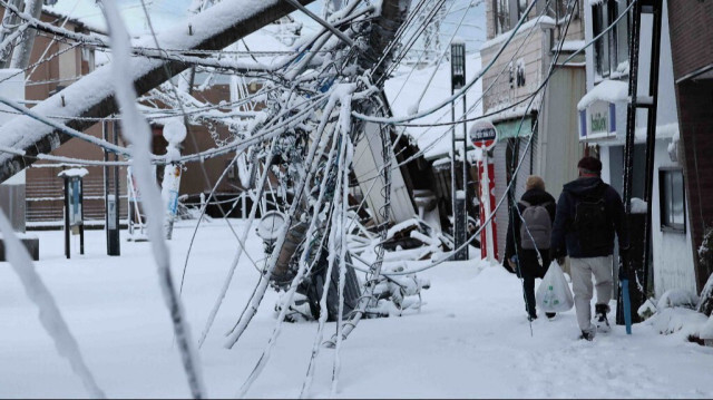 Les gens passent devant les dégâts causés par le tremblement de terre recouverts de neige dans la ville de Suzu, préfecture d'Ishikawa, le 8 janvier 2024, une semaine après le séisme de magnitude 7,5.