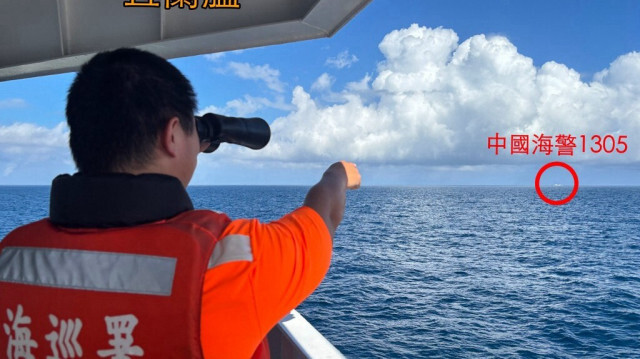 Un membre des garde-côtes taïwanais utilisant des jumelles sur un navire de patrouille au large de l'îlot Pengjia (Keelung) tout en pointant du doigt un navire des garde-côtes chinois naviguant au loin en dehors des eaux territoriales de Taïwan, le 14 octobre 2024.