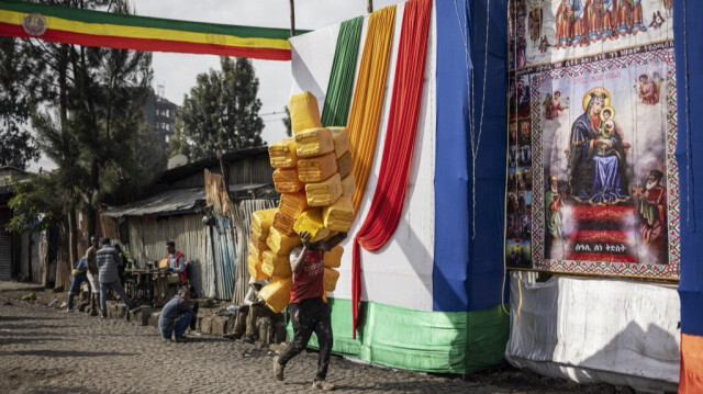 Un collecteur de déchets informel, connu en amharique sous le nom de "korale", passe devant une affiche religieuse en portant des jerrycans en plastique sur sa tête près du quartier historique de Merkato à Addis-Abeba, le 1er octobre 2024.