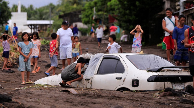 Des habitants regardent une voiture enterrée par des cendres volcaniques qui ont cascadé dans un village suite aux fortes pluies provoquées par la tempête tropicale Trami dans un village de la ville de Guinobatan, dans la province d'Albay au sud de Manille, le 23 octobre 2024.