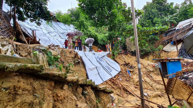 Des personnes portent des parapluies alors qu'elles se rassemblent près d'une zone touchée par un glissement de terrain dans le camp de réfugiés de Balukhali pour les Rohingyas à Ukhia à Cox's Bazar au Bangladesh, le 19 juin 2024.