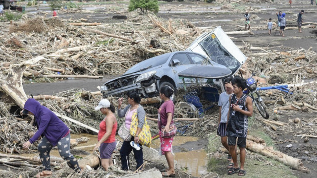 Des personnes passent devant des véhicules détruits et balayés par des débris de bois suite aux fortes pluies provoquées par la tempête tropicale Trami à Laurel, dans la province de Batangas, au sud de Manille, le 25 octobre 2024.