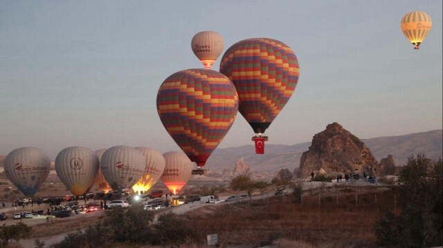 Des montgolfières survolant des cheminées de fées sur lesquelles sont accrochés des drapeaux turcs et des posters d'Atatürk lors des célébrations du 101e anniversaire de la République turque en Cappadoce, à Nevsehir en Turkyie, le 29 octobre 2024.