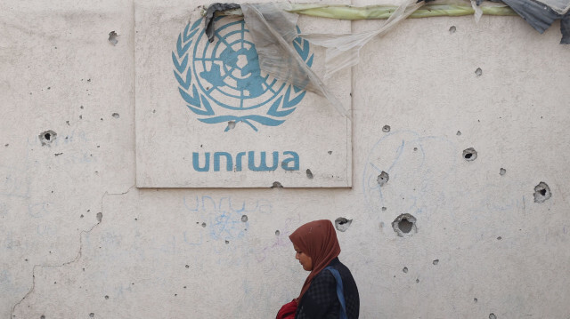 Une femme palestinienne passe devant un mur endommagé portant le logo de l'UNRWA dans un camp de personnes déplacées à Rafah, dans le sud de la bande de Gaza, le 28 mai 2024.