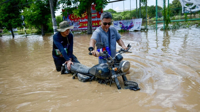 Des habitants transportent leur moto dans une rue inondée à Chiang Mai, le 6 octobre 2024.