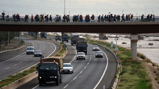 Des véhicules militaires passent sous un pont traversé par des volontaires qui se rendent dans le quartier de La Torre pour participer aux travaux de nettoyage, le 1er novembre 2024, à la suite d'une inondation dévastatrice, à Valence, dans l'est de l'Espagne.