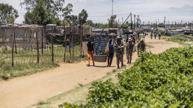 Des mineurs informels présumés, communément appelés "zama zamas" ("ceux qui essaient" en langue zoulou) portent des objets confisqués tout en étant escortés par des soldats de la South African National Defence Force (SANDF) lors de l'opération Shanela dans le quartier informel de Soul City, près de Kagiso. 