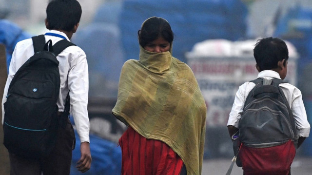 Une femme se couvre le visage alors qu'elle passe devant des écoliers par un matin froid et brumeux dans les vieux quartiers de New Delhi, le 15 novembre 2024.