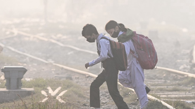 Des écoliers portant des masques traversent une voie ferrée au milieu d'un épais smog à Lahore, le 20 novembre 2024.